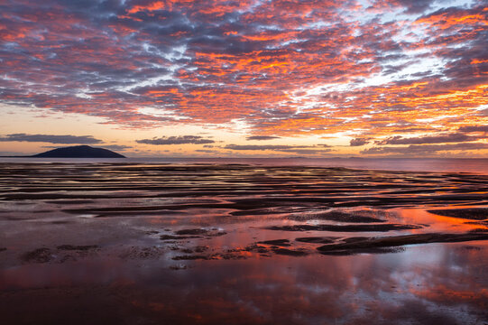 Aerial view of Saint Helens Beach at sunrise, with vibrant orange and pink clouds reflecting on the wet sand and calm ocean waters in St Helens Beach, Queensland, Australia.