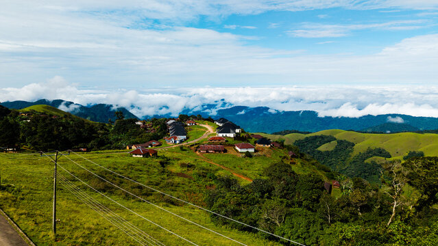 Aerial view of Obudu Mountain Resort featuring scattered lodges on a lush green hillside with rolling mountains and clouds in the background in Obudu, Cross River, Nigeria.