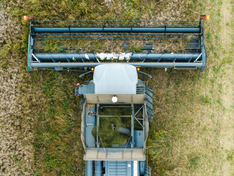 Aerial view of a combine harvester working in a field to harvest rapeseed, showing the header and grain tank from above, Talsi Municipality, Latvia.