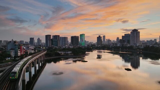 Elevated Cat Linh&ndash;Ha Dong metro train curves beside Ho Dong Da in Hanoi, Vietnam, with a calm lake, urban skyline, and colorful sunset reflections.