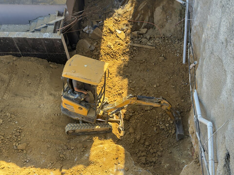 Aerial view of a small yellow excavator digging in a construction site with loose soil and rocky ground in Sariyer, Istanbul, Turkiye.