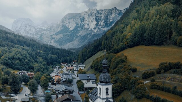 Aerial view of the Parish Church of St. Sebastian in the valley of Ramsau bei Berchtesgaden, surrounded by forests and towering Alpine peaks in Ramsau bei Berchtesgaden, Bavaria, Germany.