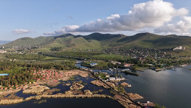 Aerial view of Lake Sevan featuring coastal wetlands, small resort buildings, and green hills under a blue sky in Sevan, Gegharkunik Province, Armenia.