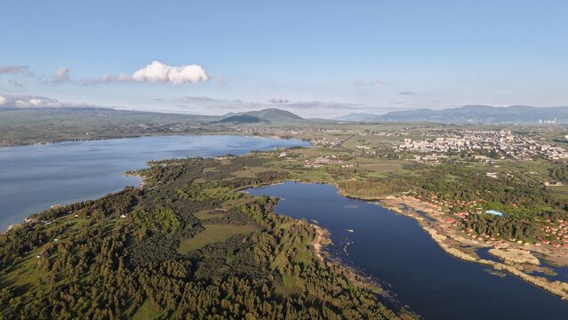 Aerial view of Lake Sevan with its expansive blue waters, surrounding lush green forests, and the urban landscape of Sevan city in Sevan, Gegharkunik Province, Armenia.