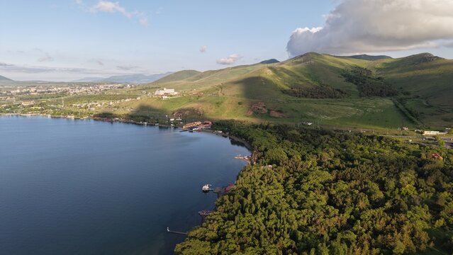 Aerial view of Lake Sevan with its expansive blue water, lush green forested shoreline, and rolling hills under a clear sky in Sevan, Gegharkunik Province, Armenia.