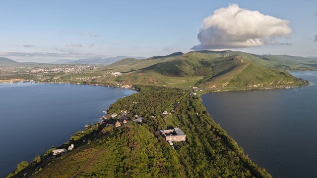 Aerial view of Lake Sevan peninsula with lush green hills, historic monastery buildings, and surrounding blue water under a clear sky in Sevan, Gegharkunik Province, Armenia.