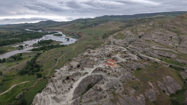 Aerial view of the ancient rock-hewn town of Uplistsikhe featuring a historic stone church, rugged sandstone formations, and the winding Mtkvari River in Kvakhvreli, Shida Kartli, Georgia.