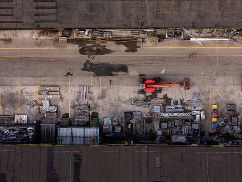 Aerial view of an industrial storage area with a red cherry picker, metal scaffolding, containers, and construction materials on a concrete lot in Gdansk, Poland.