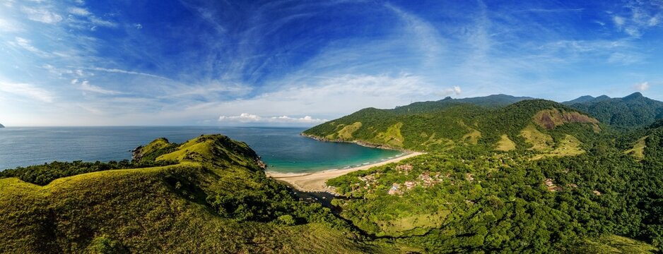Aerial view of Bonete beach with its pristine sandy shore, surrounded by lush green Atlantic Forest hills and the deep blue sea under a bright sky in Ilhabela, Sao Paulo, Brazil.