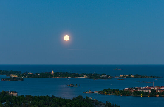 Aerial view of the full moon rising over the Helsinki archipelago with calm sea and islands at twilight in Helsinki, Uusimaa, Finland.
