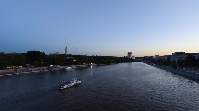 An evening city view of the river with a motor vessel sailing along it