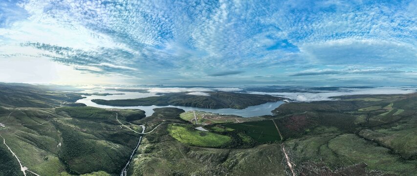 Aerial view of Serra da Canastra featuring rolling green hills, a large reservoir, and scattered clouds over the landscape in Sao Roque de Minas, Minas Gerais, Brazil.