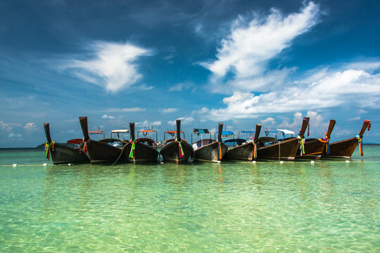 Aerial view of traditional Thai long-tail boats moored in the clear turquoise waters of Pattaya Beach under a bright blue sky in Pattaya, Chon Buri, Thailand.