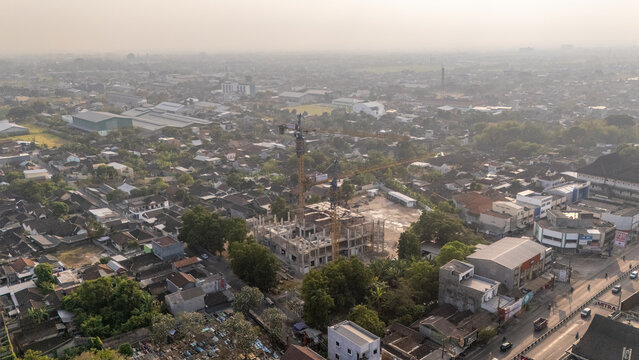 Aerial view of a construction site with cranes rising above a dense urban landscape of residential rooftops and buildings in Surakarta, Central Java, Indonesia.