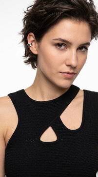 Close-up portrait of edgy brunette woman with pixie haircut and silver ear cuff in black cut-out top
