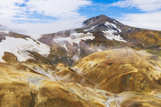 Aerial view of Kerlingarfjoll mountain range with geothermal steam, snow patches, and colorful rhyolite slopes in Hrunamannahreppur, Iceland.