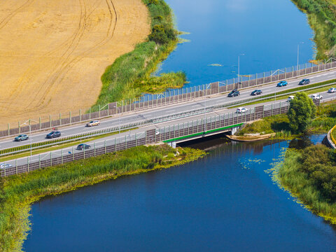Aerial view of S7 Expressway with cars driving on the bridge over a river, surrounded by green fields and vegetation in Nowy Dwor Gdanski, Pomeranian Voivodeship, Poland.