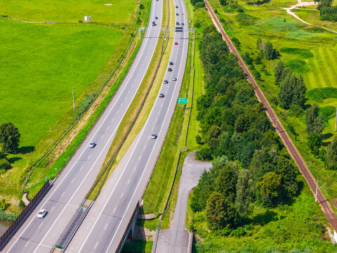 Aerial view of the S7 Expressway cutting through green fields and forests with a railway line running parallel in Nowy Dwor Gdanski, Pomeranian Voivodeship, Poland.
