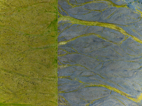 Aerial view of the striking contrast between vibrant green grassy fields and dark volcanic riverbeds in the Icelandic landscape, Iceland.