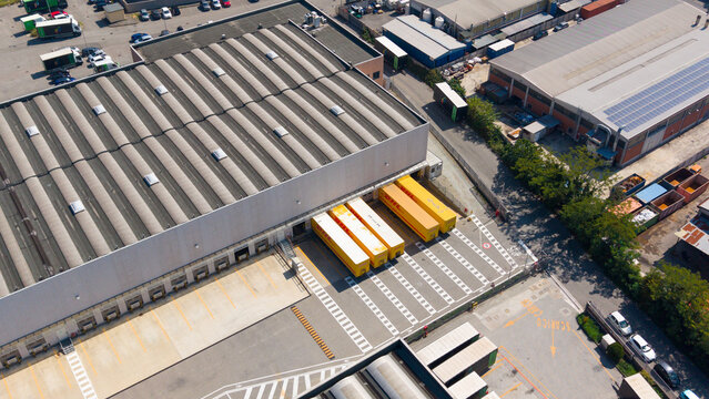 San Giuliano Milanese, Italy - 04 September 2026: Aerial view of the DHL Express facility with yellow delivery trucks parked at the loading bays of a large industrial warehouse.