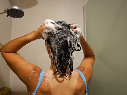Woman washing hair in shower with shampoo and foam