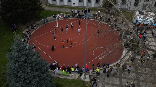 Valjevo, Serbia - 12 April 2025: Aerial view of a basketball game in progress on a circular red court with spectators sitting on the surrounding stone steps in Valjevo.