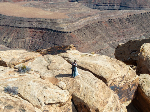 Utah, United States - 16 March 2025: Aerial view of a couple embracing on a rocky cliff edge overlooking a vast desert canyon landscape with layered rock formations under bright daylight.