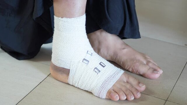 Close up of person with white bandage around injured ankle sitting on floor in pain