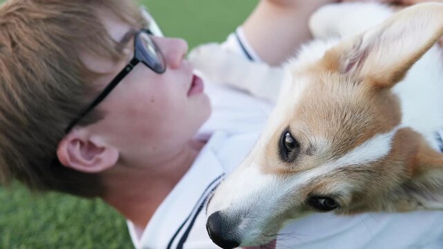 Man lying on the lawn with his corgi, relaxing together in nature and expressing joy and companionship.