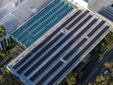 Wantirna South, Victoria, Australia - 03 September 2026: Aerial view of a building roof covered with solar panel arrays and a glass atrium, surrounded by trees and a road.