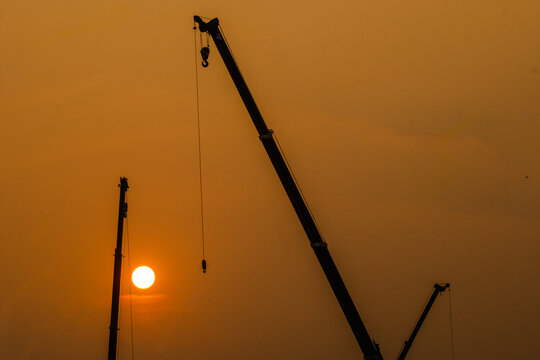 Construction cranes silhouetted against a dramatic sunset or sunrise sky