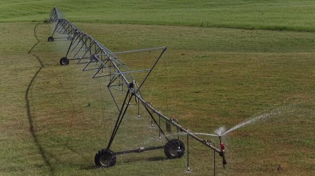 Automated center pivot irrigation system operating on green farmland agricultural field.