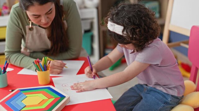Woman teacher guiding girl drawing with hand on paper at a bright classroom building, using colored pencils and wooden toy blocks visible; focused learning.
