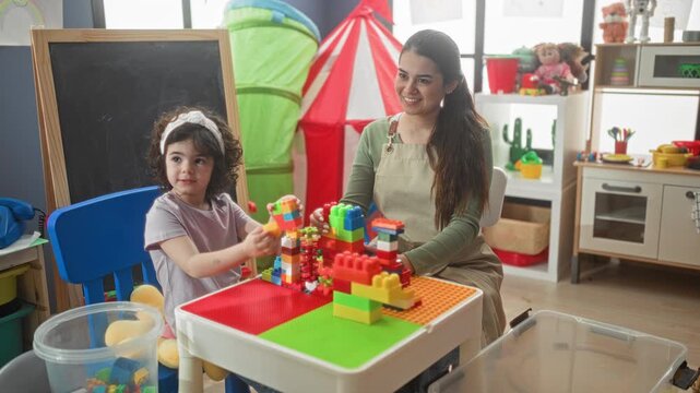 Woman teacher builds colorful block tower with child at play table in building; nurturing joy learning.