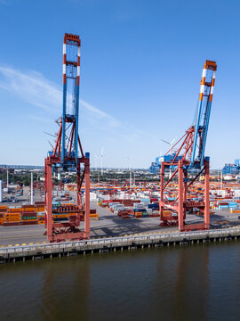 Hamburg, Germany - 24 June 2026: Aerial view of Container Terminal EUROGATE with large gantry cranes, rows of shipping containers, and wind turbines under a clear blue sky.