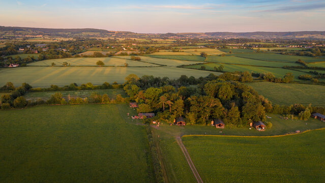 Newton Valance, United Kingdom - 21 June 2026: Aerial view of Feather Down Moor Farm nestled in the lush green countryside with small wooden cabins surrounded by trees at sunset.