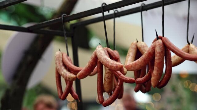 Sausages hanging on hooks at outdoor christmas market stall. Traditional smoked sausages for sale on street food festival. Festive winter holiday market food concept