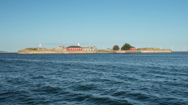 Historic Trekroner Fort stands on an island in Copenhagen harbor in Denmark. Danish sea fortress serves maritime defense history and heritage tourism. Ocean waves ripple under sunny blue sky.