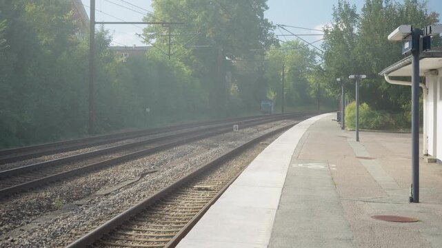 Empty railroad platform stands beside railway tracks on a foggy morning. Misty suburban train station serves passenger transit. Early commuter journey begins along transit infrastructure.