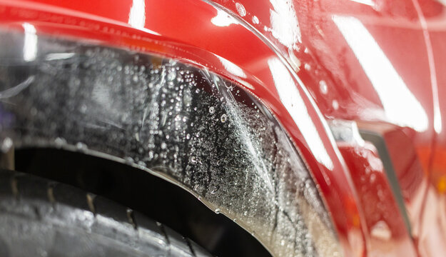 Clear polyurethane paint protection film PPF with water soap bubbles applied on a red metallic car fender wheel arch. Vehicle bodywork wrapping, anti-scratch shielding, and paint protection car. 