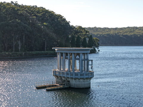 Silvan, Victoria, Australia - 01 September 2026: Aerial view of the concrete intake tower at Silvan Reservoir Park surrounded by deep blue water and dense forest under a clear sky.