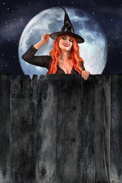 Red-haired witch in black hat peeking from behind dark wooden fence with empty copy space against the backdrop of the moon and night sky. Halloween holiday mockup for text or advertising design