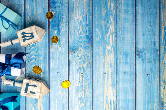 Hanukkah background. Dreidel, with blue lettering נ&lrm; nun, ג&lrm; gimel, ה&lrm; hei, ש&lrm; shin, gift boxs, gold coins on wooden background. Jewish holiday of Hanukkah.