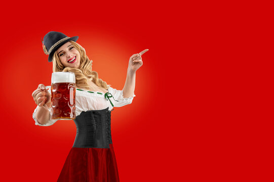 Oktoberfest girl waitress pointing finger at empty copy space. Woman in dirndl, tyrolean hat serving a mug of beer for Bavarian German or Austrian beer party, autumn festival