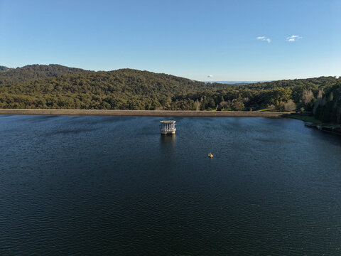 Silvan, Victoria, Australia - 01 September 2026: Aerial view of Silvan Reservoir Park, featuring the central valve tower, calm water, and surrounding dense forest under a clear sky.