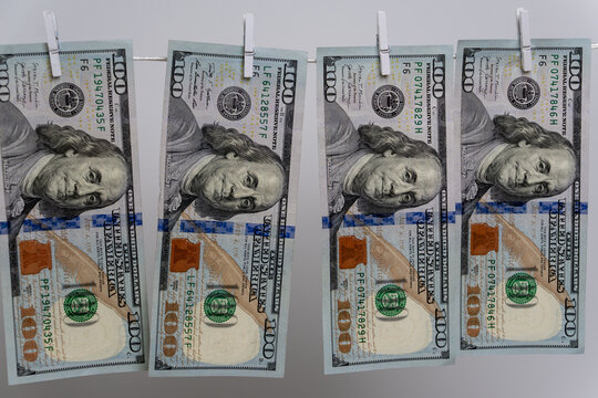 Four one hundred US dollar bills hang on white rope with wooden clothespins against gray background, symbolizing money laundering, financial crime, and shadow economy.