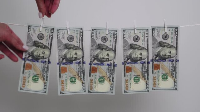Female hand hangs US hundred dollar banknote with wooden pin on a clothesline, illustrating money laundering.