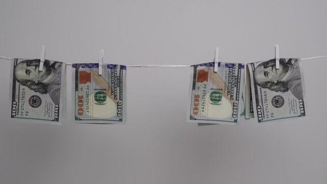 Female hand reaches to take folded US hundred dollar banknote off a clothesline, illustrating money laundering.