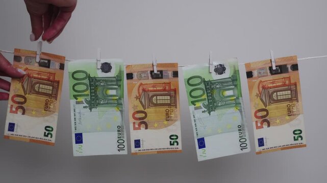 Female hand hangs euro banknote with a wooden pin on a clothesline, illustrating money laundering concept.