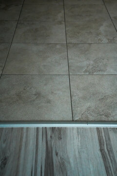 Beige ceramic floor tiles meeting wooden flooring with a metal transition strip in a home interior